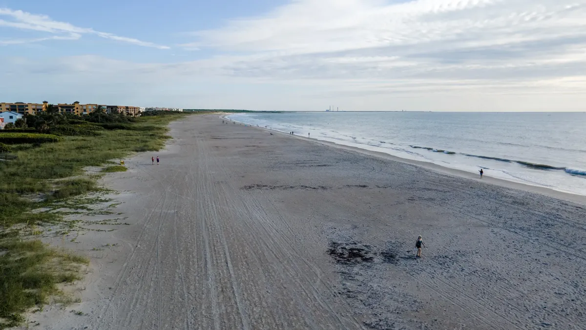 Aerial view of a tranquil beach scene with distant people and gentle waves.