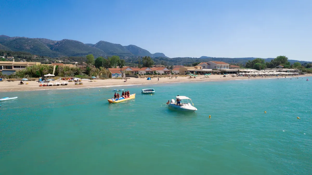 Aerial view of a lively beach in Corfu, Greece, featuring boats and vibrant summer activities.
