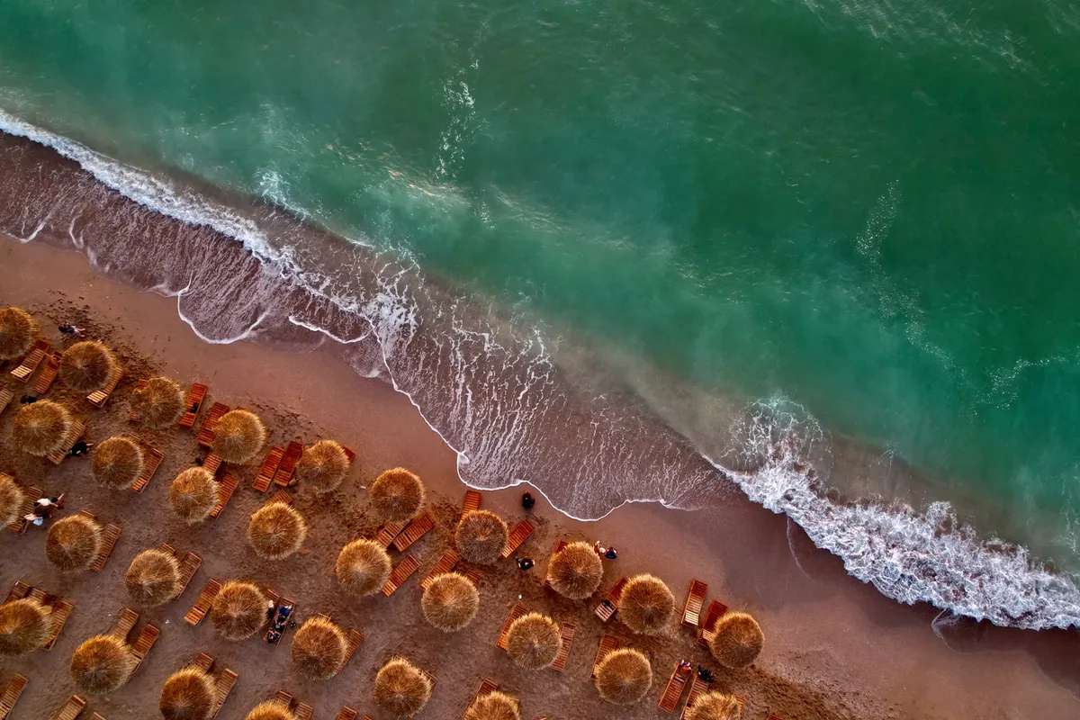Aerial view of a tropical beach with thatch umbrellas and waves crashing on the shore.