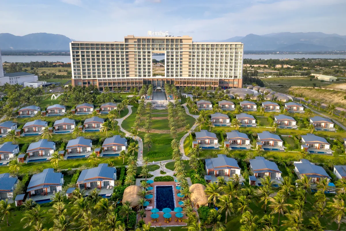 Aerial view of a luxury resort with bungalows surrounded by mountains and palm trees.